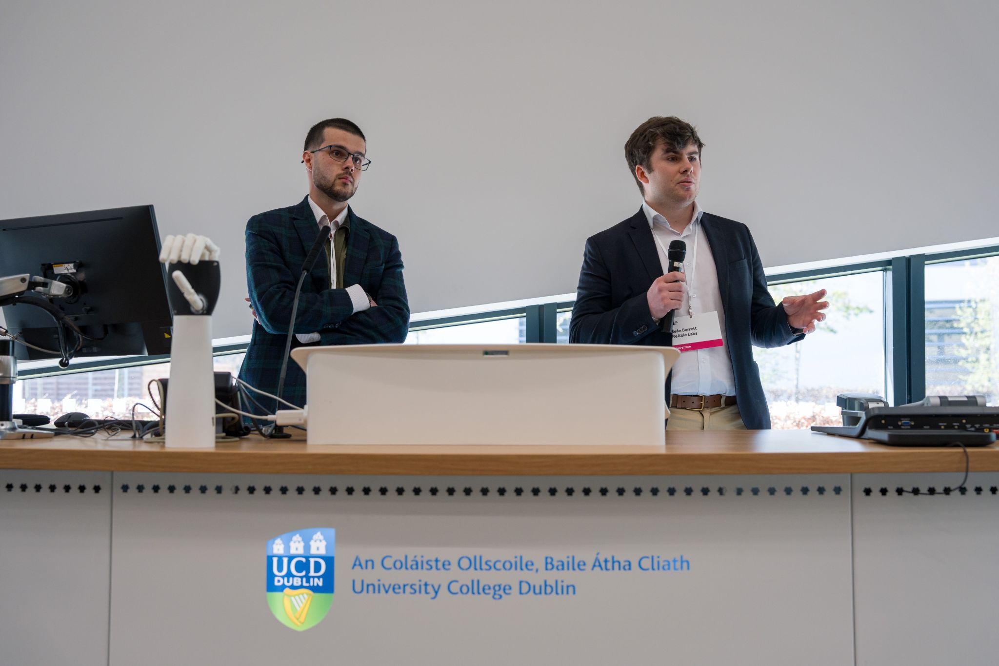 Sean Barrett pitching ReAble Labs on stage at UCD with William Hartley and the prosthetic hand beside him